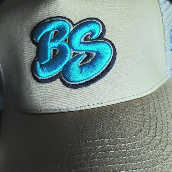 Slow pan across the Bradford Sports Essential trucker hat in beige with teal BS embroidery