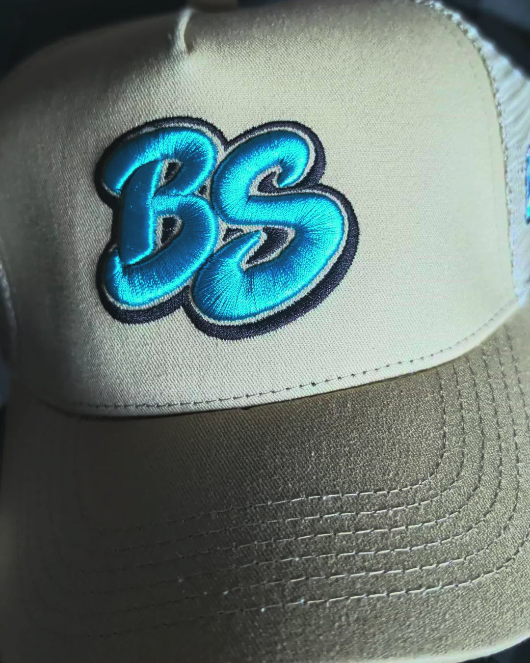 Slow pan across the Bradford Sports Essential trucker hat in beige with teal BS embroidery
